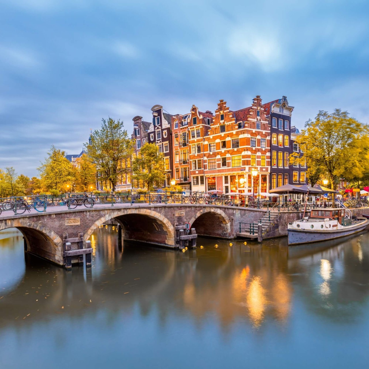 A blue canal in Amsterdam, crossed by a bridge, with tall, old-style houses in the background