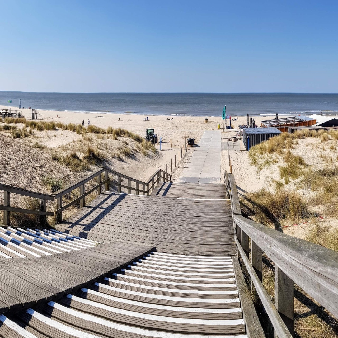 Wooden steps leading down to a beach with white sand and the ocean in the background