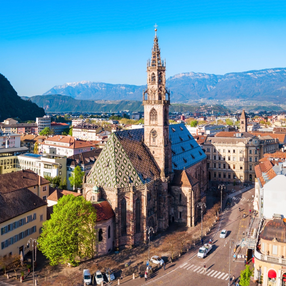 An aerial view of Bolzano's cathedral, with buildings and mountains in the background