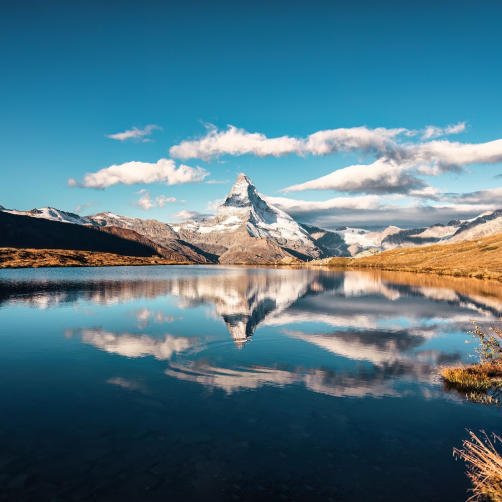 A view of an alpine lake with the sharp peak of the Matterhorn reflected in the surface