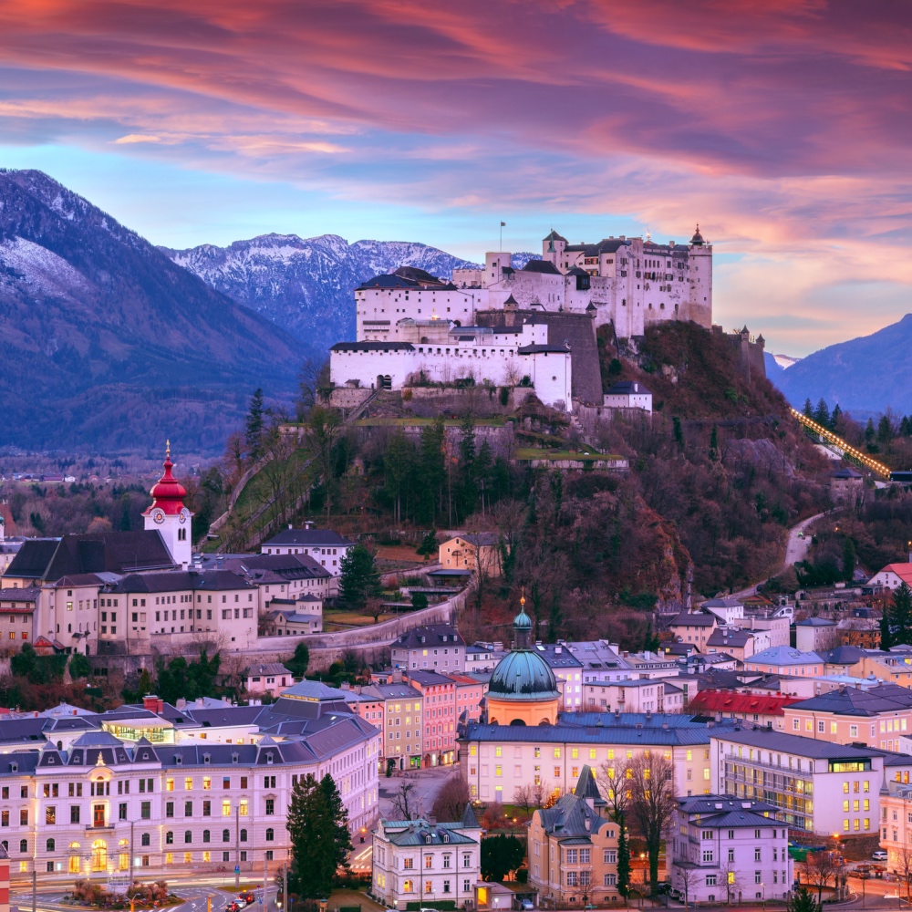 An aerial view of Salzburg's castle perched on a high hill over the city during a pink sunset